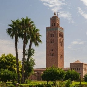 An iconic Moroccan minaret towers over lush gardens under a clear blue sky.